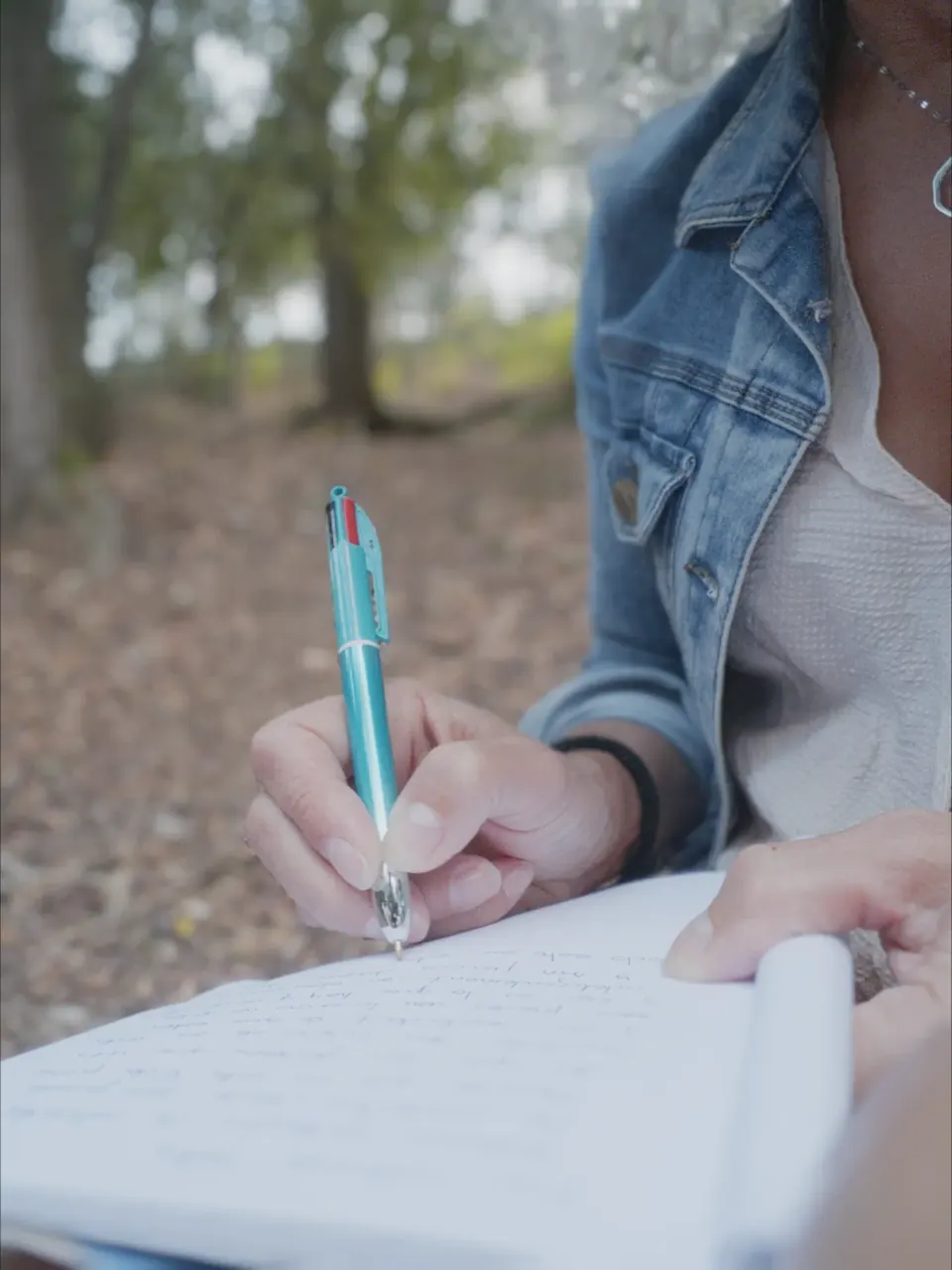 Una mano escribe en un cuaderno al aire libre